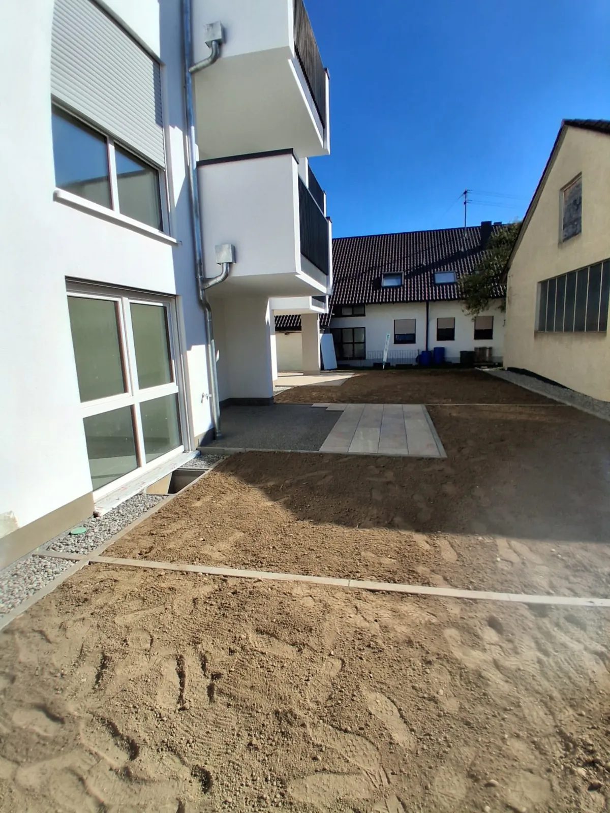 Planierter Hof mit Plattenfläche und Bordsteinen an einem Neubau-Wohnhaus